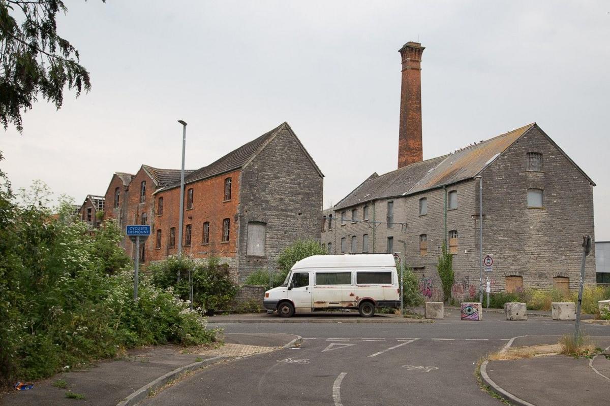 An old white transit van outside brick buidlings