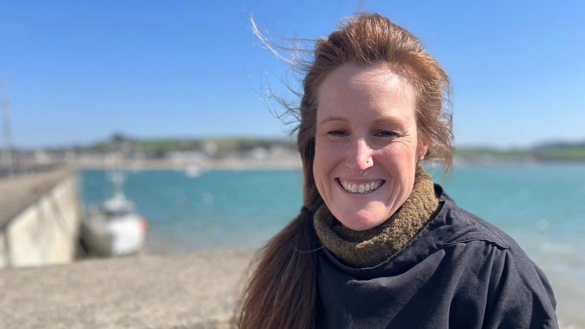 Kym Harris in a rollneck jumper and a fisherman's smock with a blurred background of the estuary 