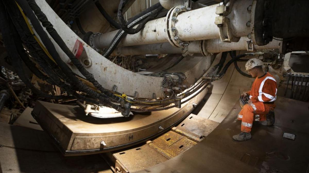 A man in an orange overall and white hard hat sat in a tunnel using machinery