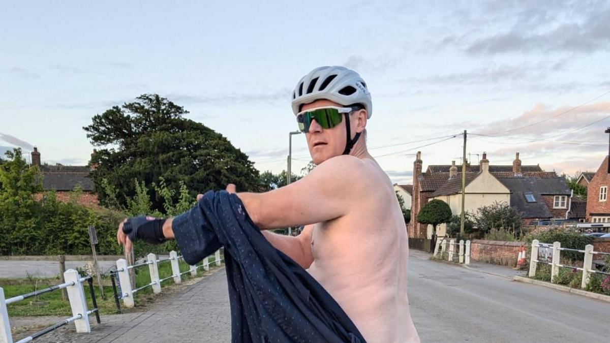 Pictured is one of the participants of the calendar, Dan Smith. He is wearing his cyclist glasses and a helmet but his topless after removing his jersey. 