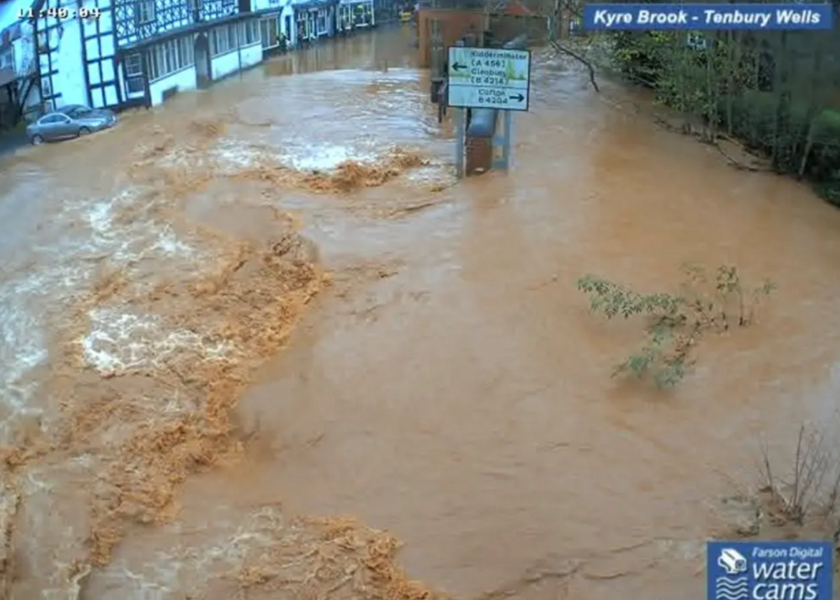 Brown water rises in a town centre and reaches halfway up a single street sign in the middle of the flow, while water also laps at the foot of buildings in the distance