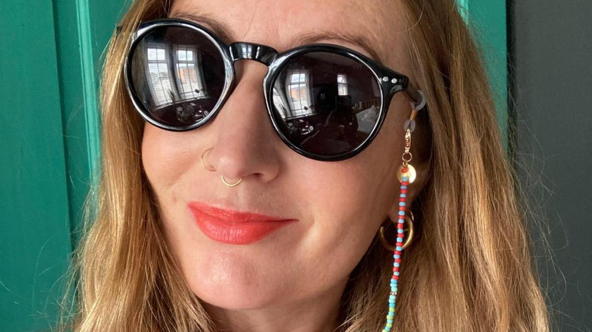 Lowri smiling and wearing dark glasses and bright lipstick. 