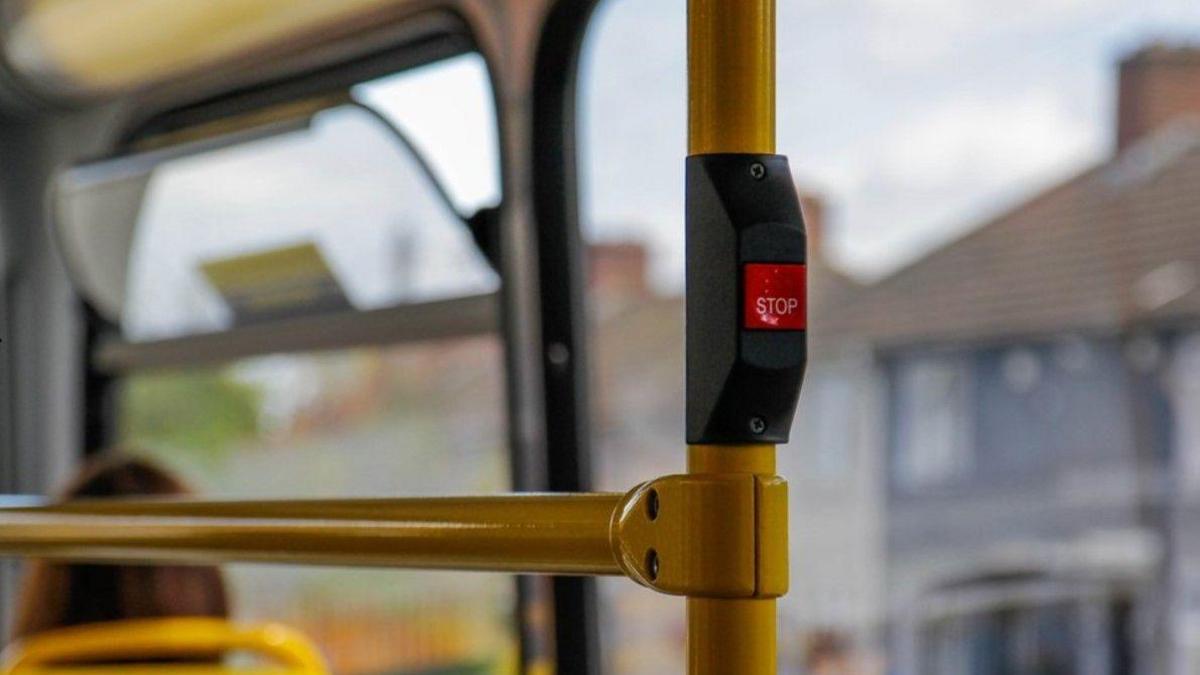 A generic image taken from inside a bus features a stop button. Houses visible through windows in the background are blurred.