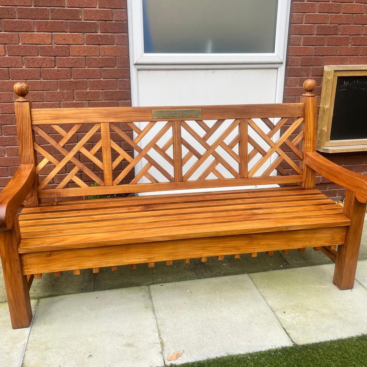 A wooden bench on a path in front of a building with a white window.
