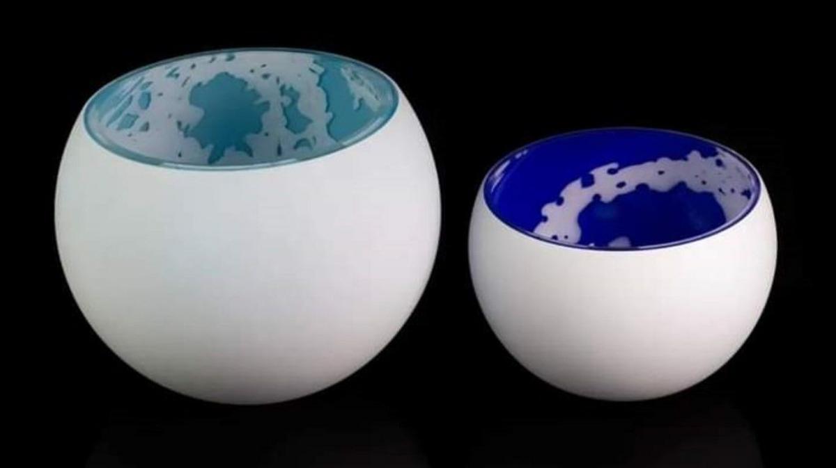 Two examples of Zoe Johnston's glass-blowing work, consisting of two white, high sheen glazed, bowls. The large one is decorated with a turquoise and white interior, with the smaller one of a similar design, but using electric blue colour. 