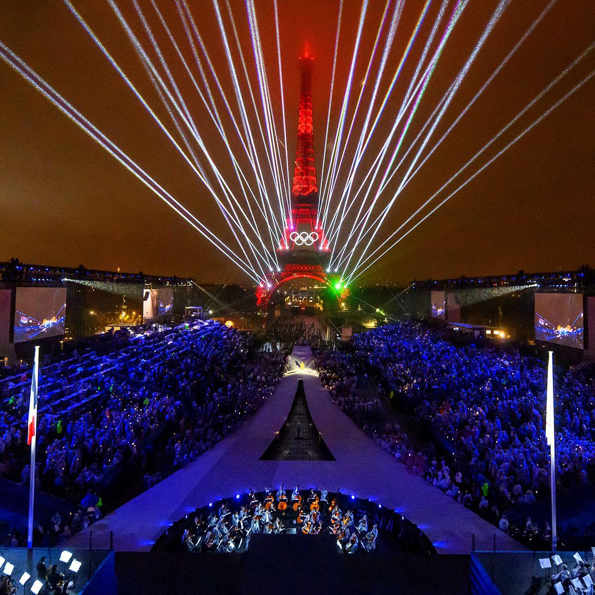 Lights and lasers fill the night sky over the Trocadero venue, with the Eiffel Tower looming in the background and audience members in the foreground, during the opening ceremony of the Paris 2024 Olympic Games