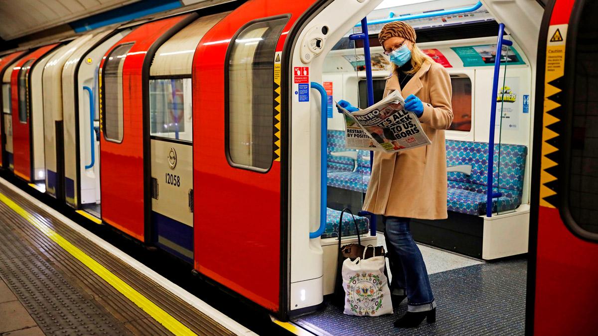 A woman wearing a mask reads a newspaper on a London Underground train, 11 May 2020