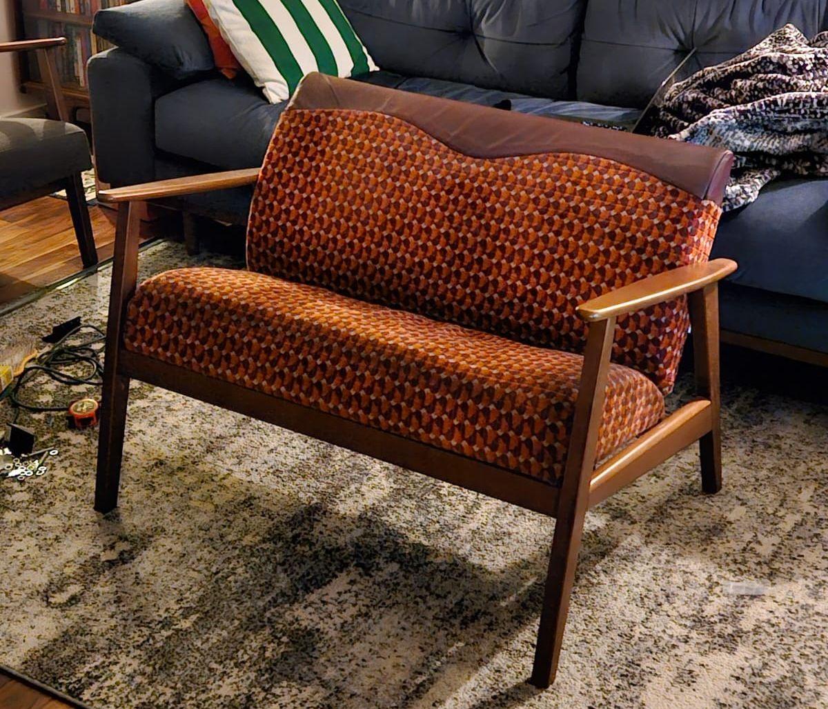 A bright orange and red subway seat converted into a couch with wooden armrests and legs in a living room.