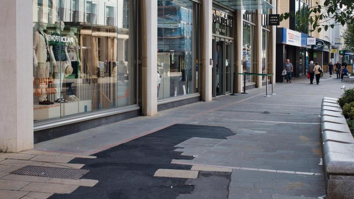 Black patched of tarmac in the pavement outside John Lewis in Cheltenham town centre. 