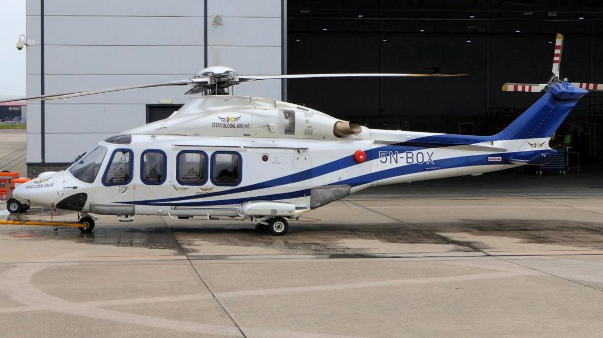 White 5-seater helicopter with blue lines standing at an airport