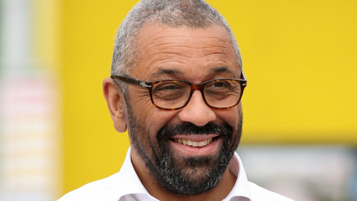 Headshot of a smiling James Cleverly, wearing a white shirt and tortoiseshell glasses 