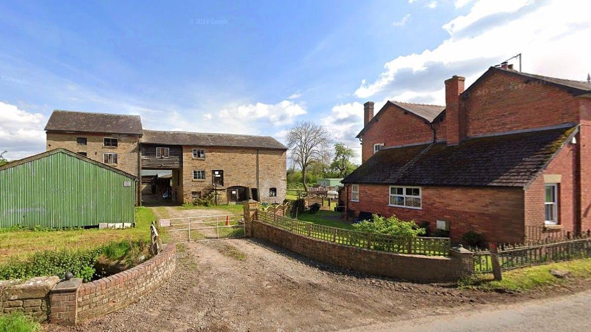 A historic flour mill, pictured next to a large red brick house surrounded by grass, fencing and a brick wall.