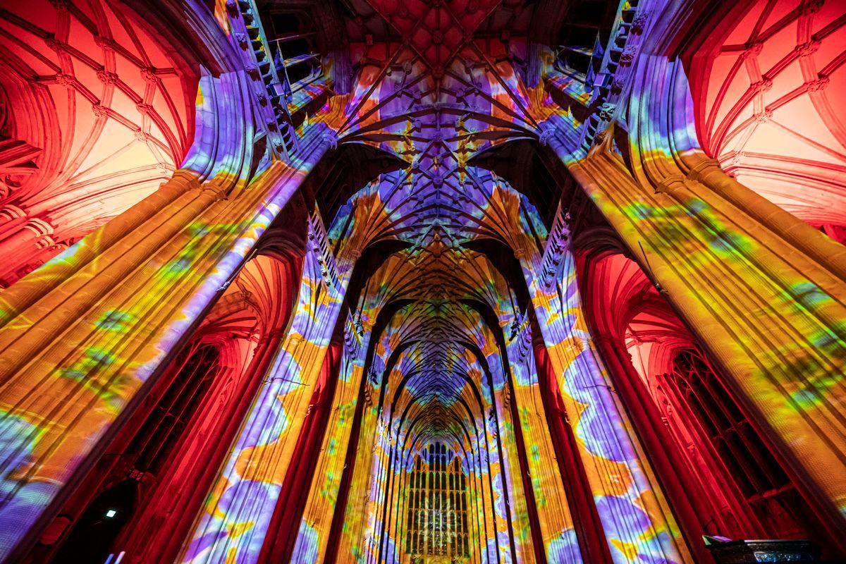 Multi-coloured installation projected onto Gloucester Cathedral's walls as the building is lit up at night.
