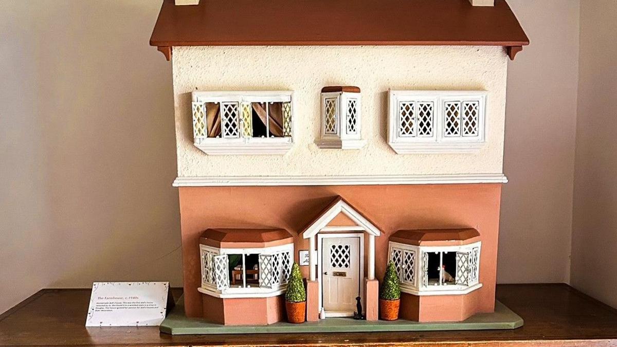 A single dolls house in cream and terracotta with white lattice windows and a brown roof, which has been placed on a wooden table. 