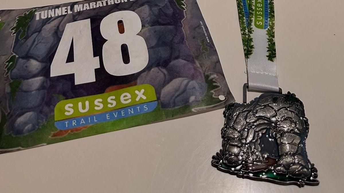 A race number and a medal, both bearing the image of a stone tunnel or cave entrance.