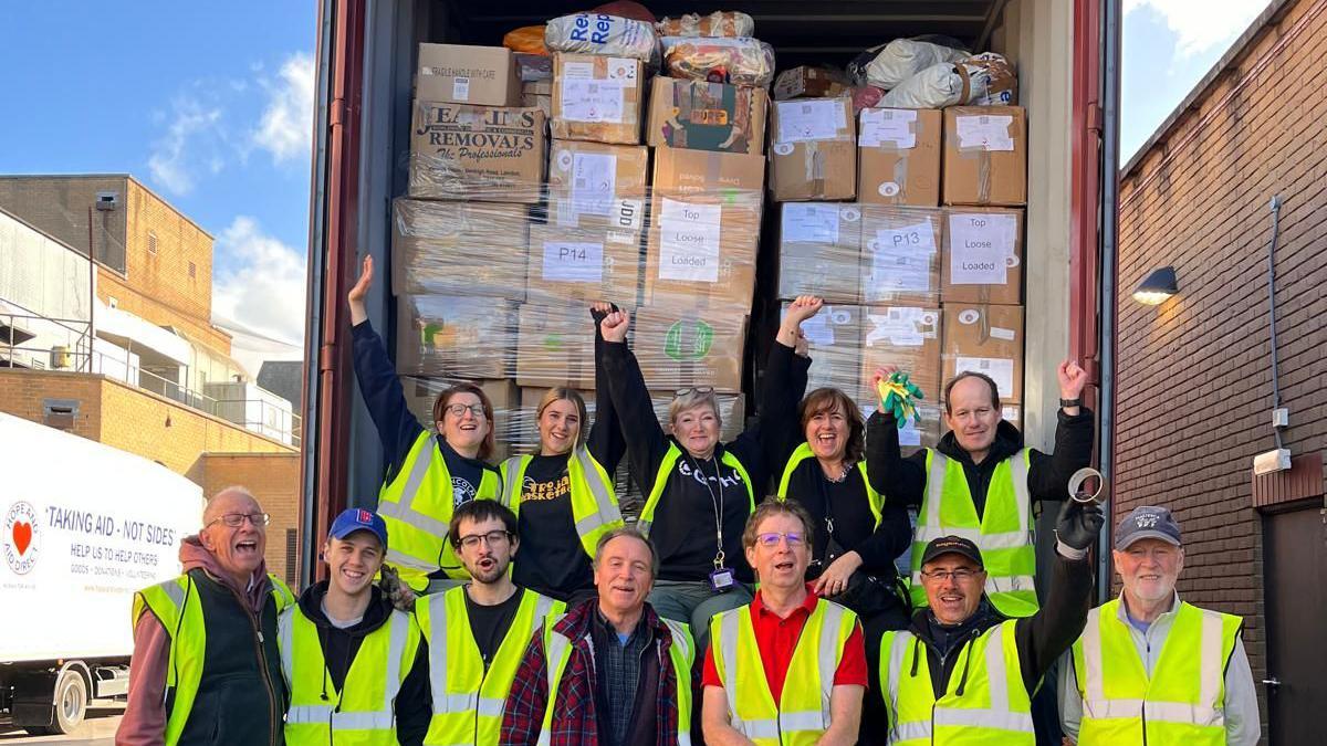 Several volunteer standing in front of a lorry packed with aid