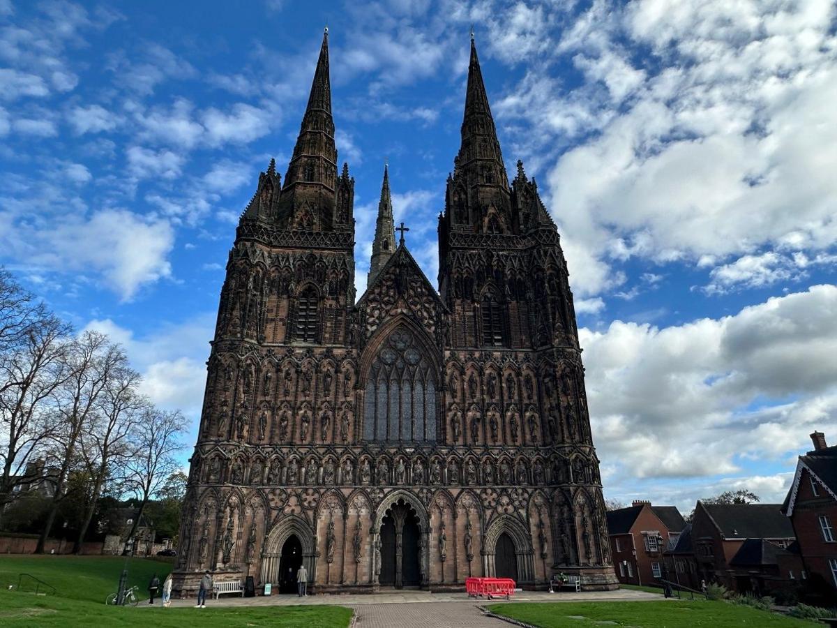 A cathedral with huge spires and stone gothic arches sits under a blue sky with some white clouds.