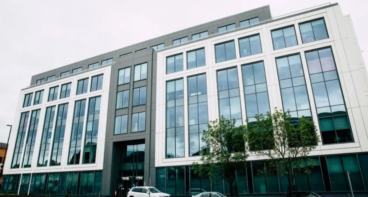 Grey and white office building with large glass windows  and two green trees outside.