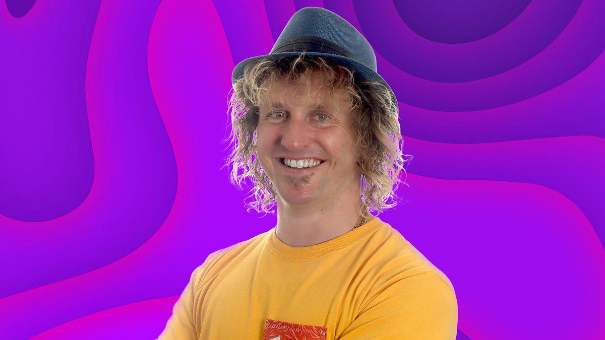 Rob Jelly, who is wearing a hat and yellow T-shirt. He is standing in front of a purple background.