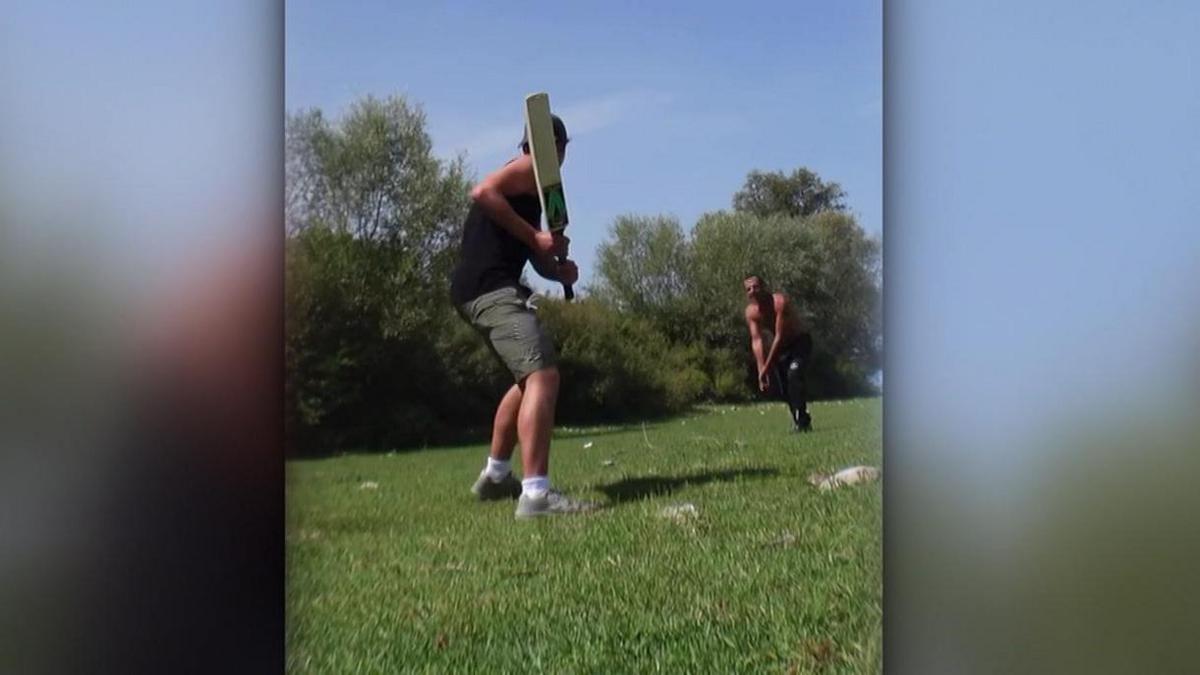 Tommy plays cricket with another man in a field.