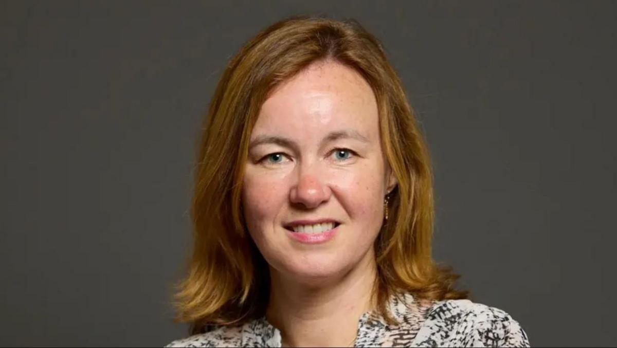 Woman with brown hair and a black and white top looking directly at the camera. She has brown hair and is smiling.