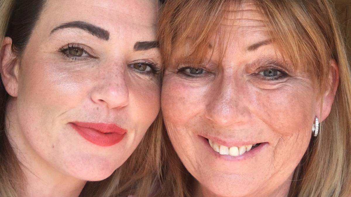 Therese Roberts (right) with her daughter Lindsay (left). They are both smiling and looking into the camera. Lindsay has bright red lipstick on and Therese has a silver earring in her ear. 