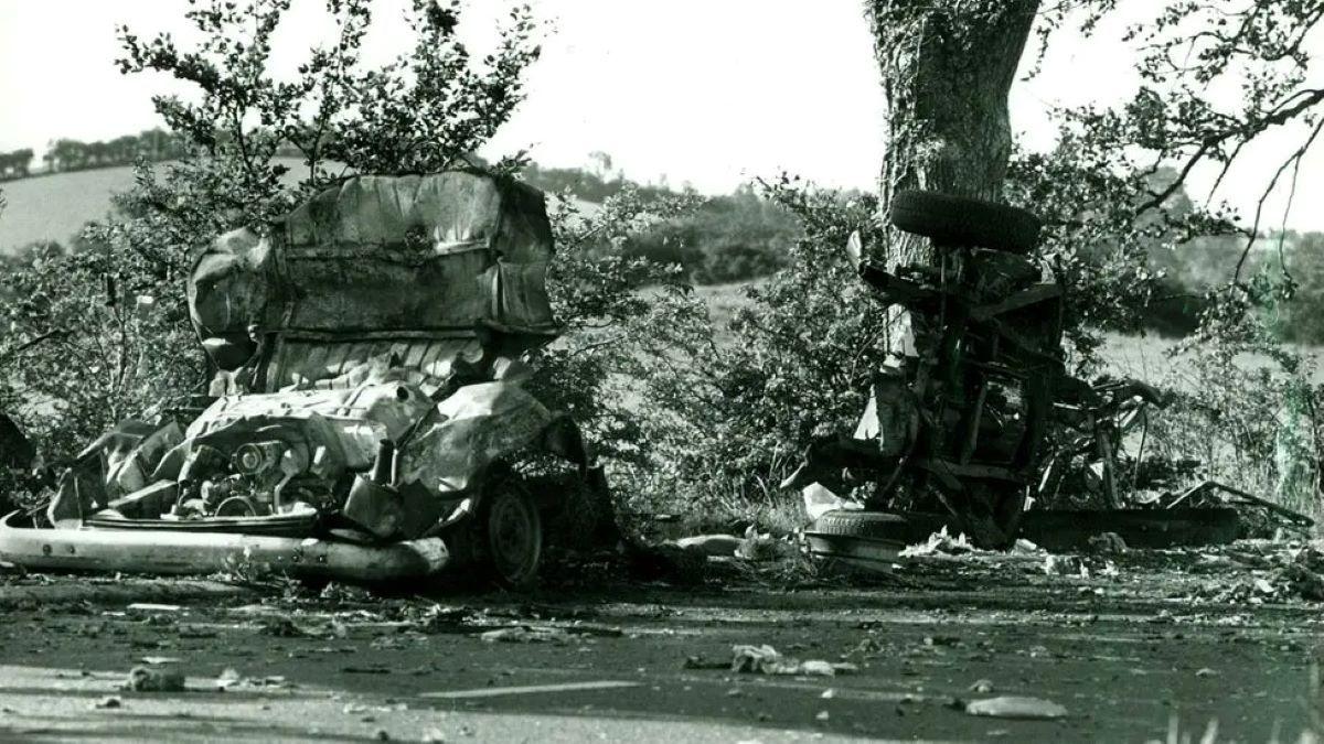 A black and white image of the mini bus which was blown up. It is in two pieces as the main body of the vehicle lies on one side of the road and the wheels on the other.