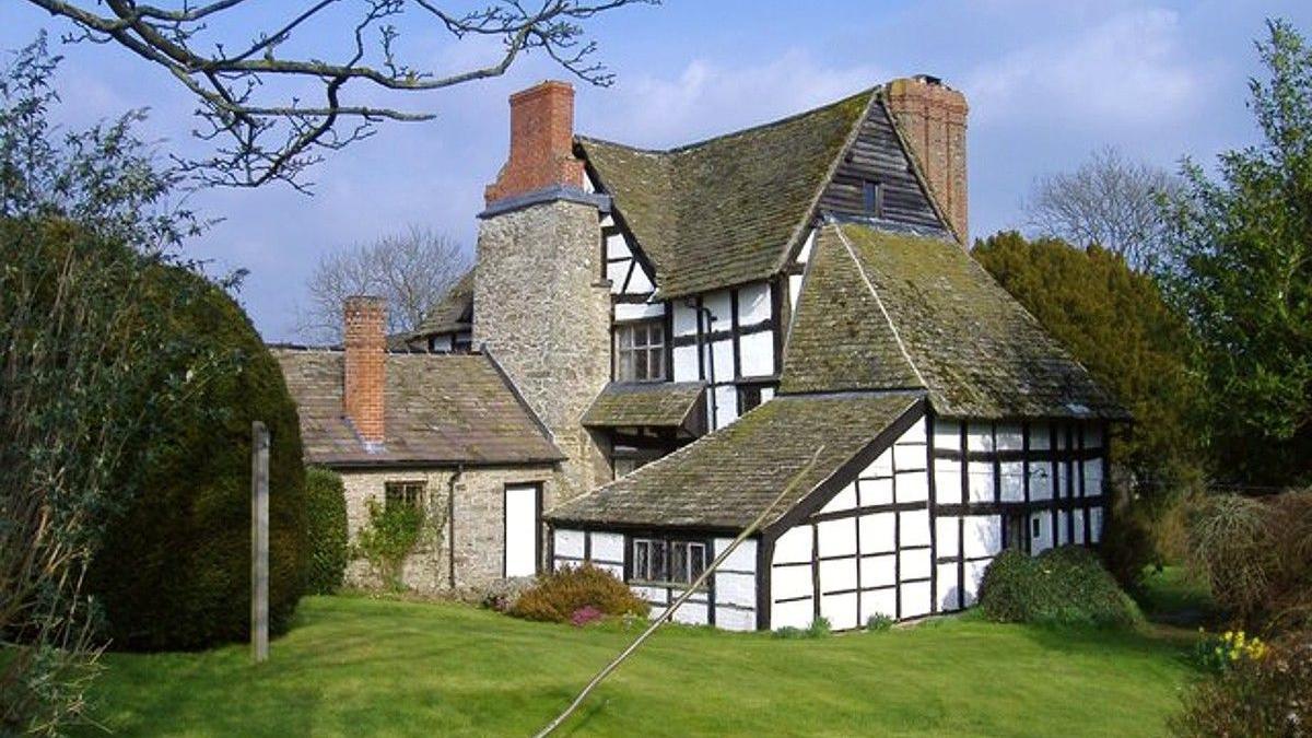 A black and white farmhouse with a green lawn and bushes, with a blue sky overhead