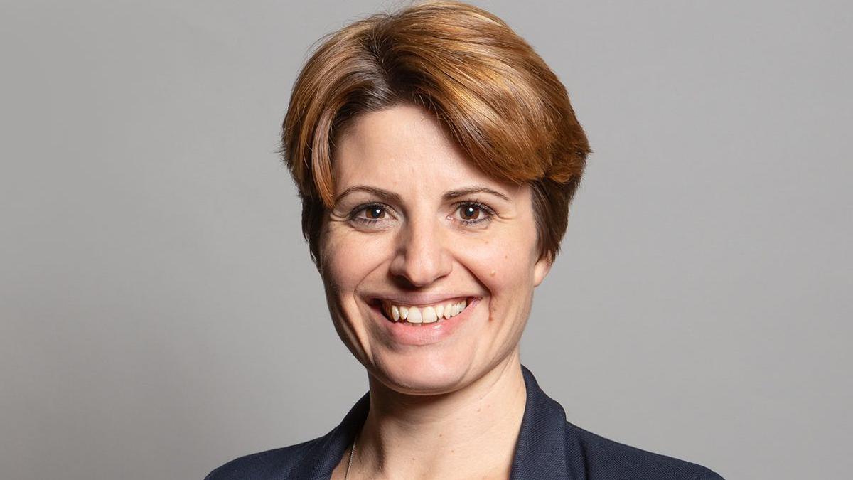 Official portrait of Emma Hardy, who has medium length brown hair and is standing in front of a neutral grey background.
