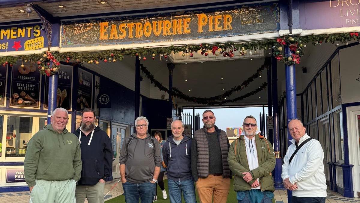 Seven men standing in front of Eastbourne Pier.