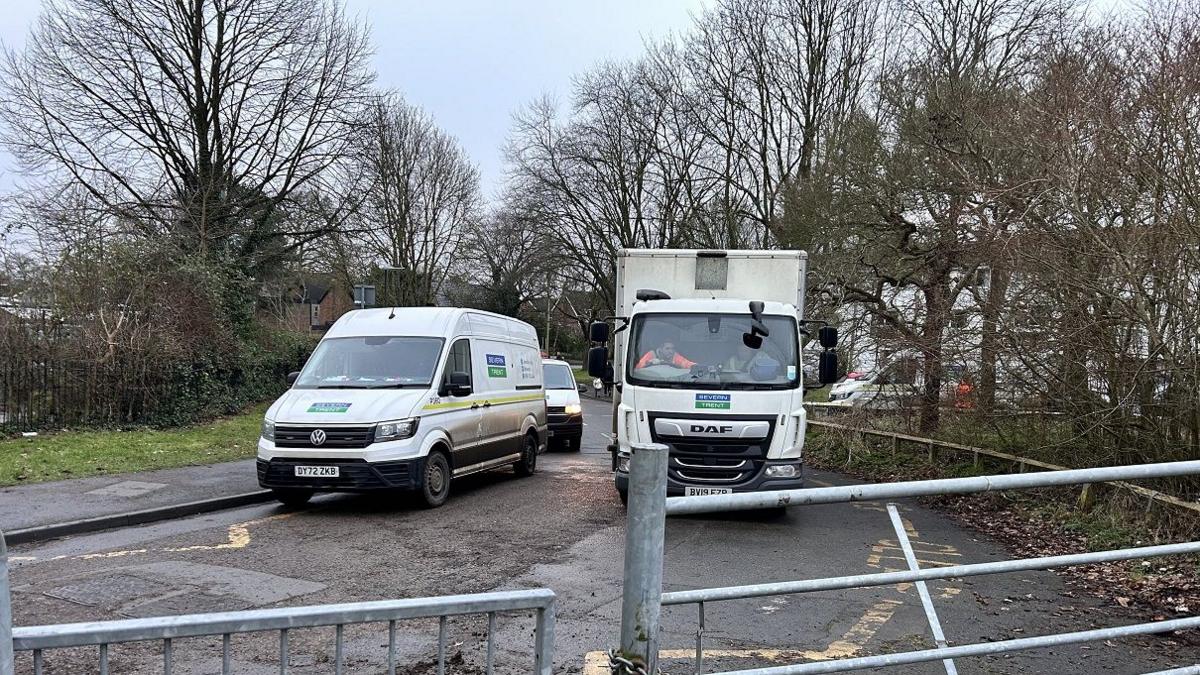 Three white vans with the blue and green Severn Trent water logo are parked on a road in front of a metal gate.