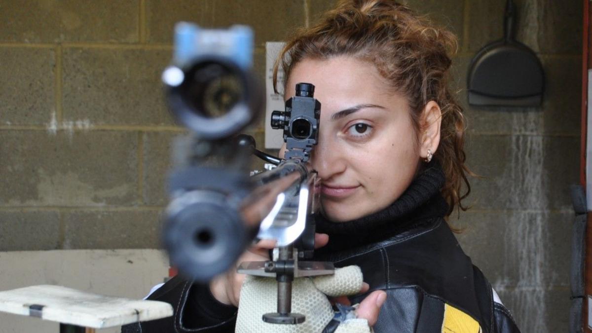 Sakina Mamedova aiming a rifle directly at the camera. She has her hair tied back. 