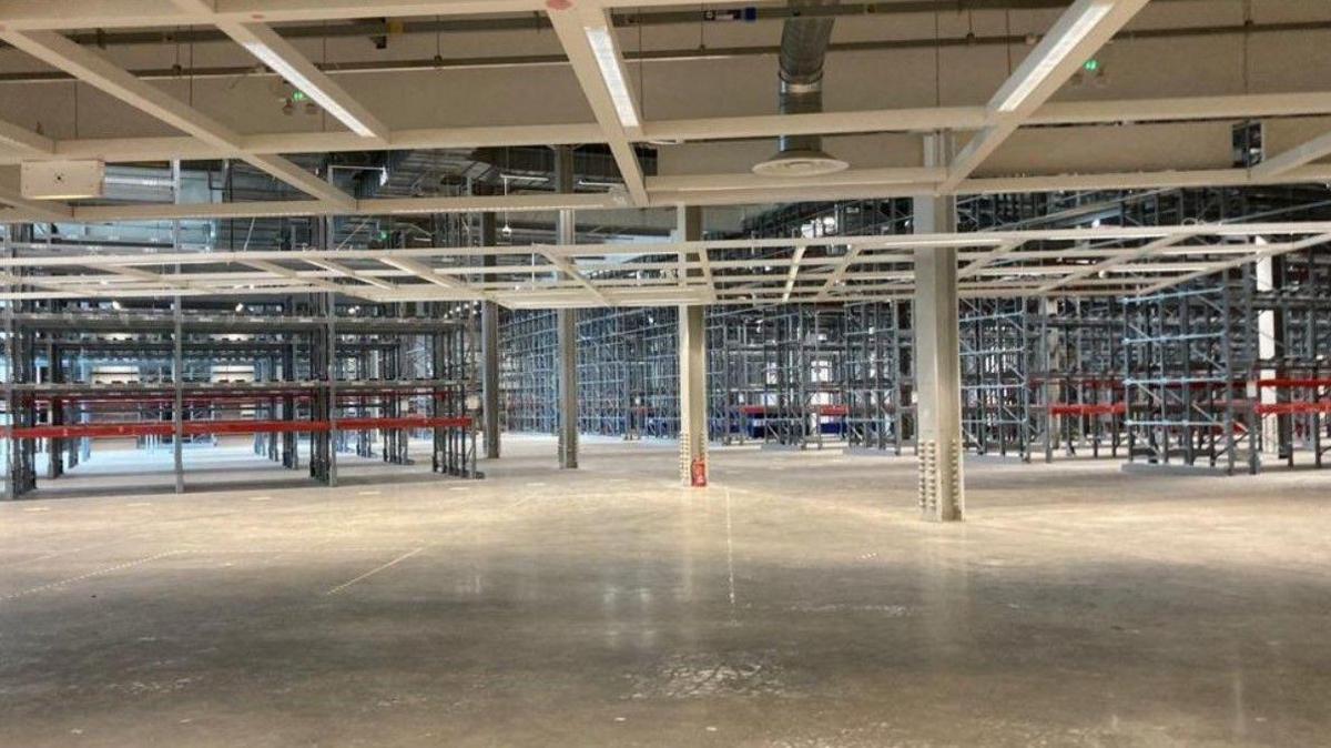 Inside the former Ikea building, showing lines of huge, empty shelving and grey concrete floor