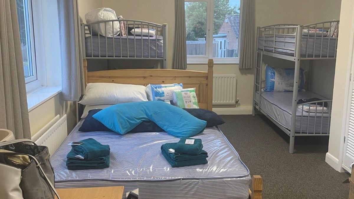 A small bedroom which contains three beds - one double and two bunk beds. The beds are not made, with towels and bags of bedding in piles.