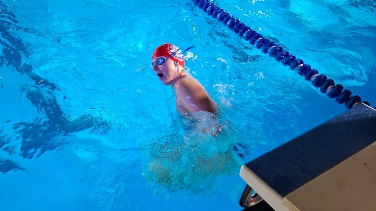 Helen Hislop is pictured swimming in an outdoor pool. She has a swimming cap and goggles on.