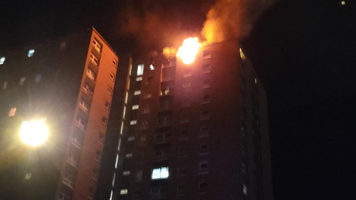 Flames coming out of the16th floor of Twinnell House in Bristol after an e-bike started a fire. The building is seen on a dark night from street level, with some windows illuminated by internal lights