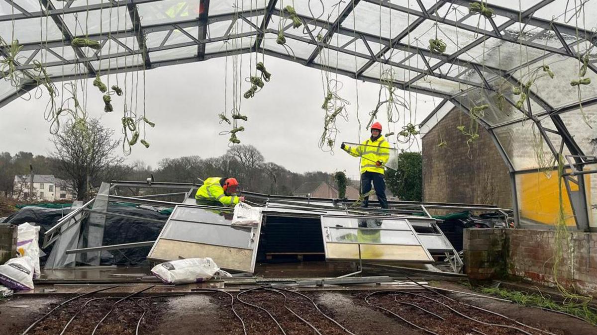 Two people wearing high vis jackets stand on large piles of glass 