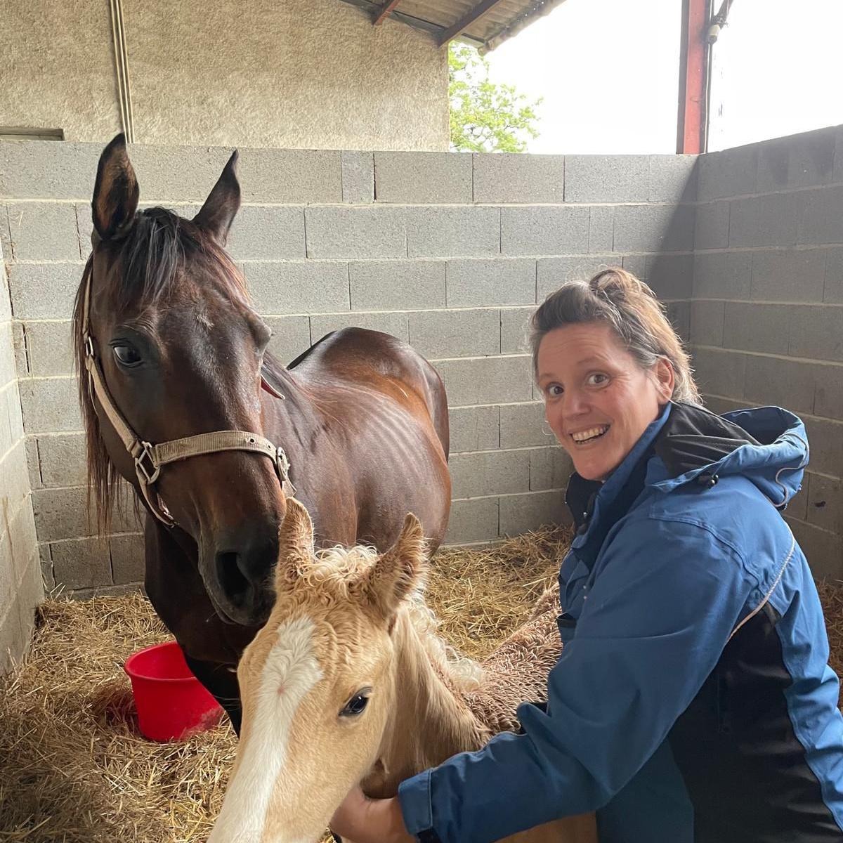 A photograph of Corinne smiling with two horses next to her