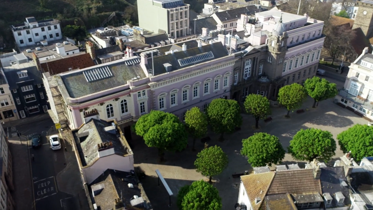 An aerial view of Jersey buildings from above in St Helier, with a walkway surrounded by green trees in the middle.