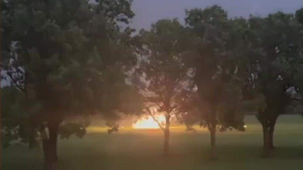 A glowing ball of flame filmed from a distance on a grassy field beyond a line of trees