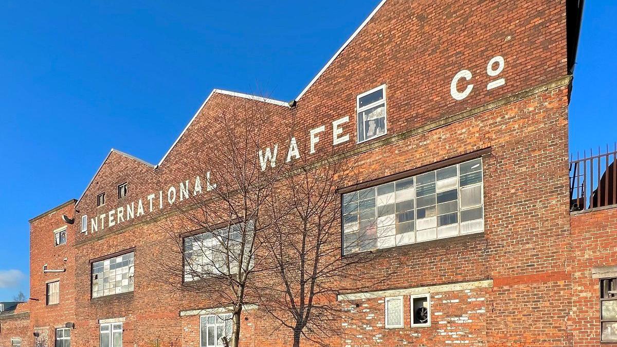 Progress Works, Ayres Road, Old Trafford, a red brick building with a tree in the foreground on a sunny day with the words 'international wafe co' emblazoned on the front of the building, 