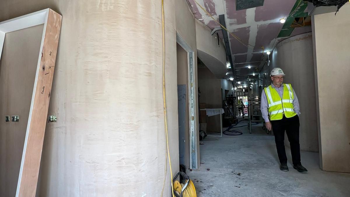 A corridor in a diagnostic centre where construction work is under way. Plaster can be seen on the walls and a man in a hard hat and high vis jacket is on the right of the photo 