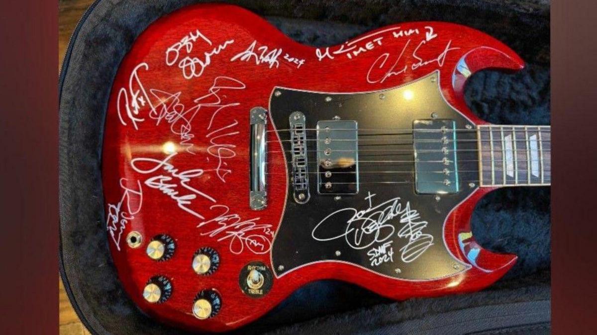 A red electric guitar that has been signed by several people, including Ozzy Osbourne, with their names being in white.
