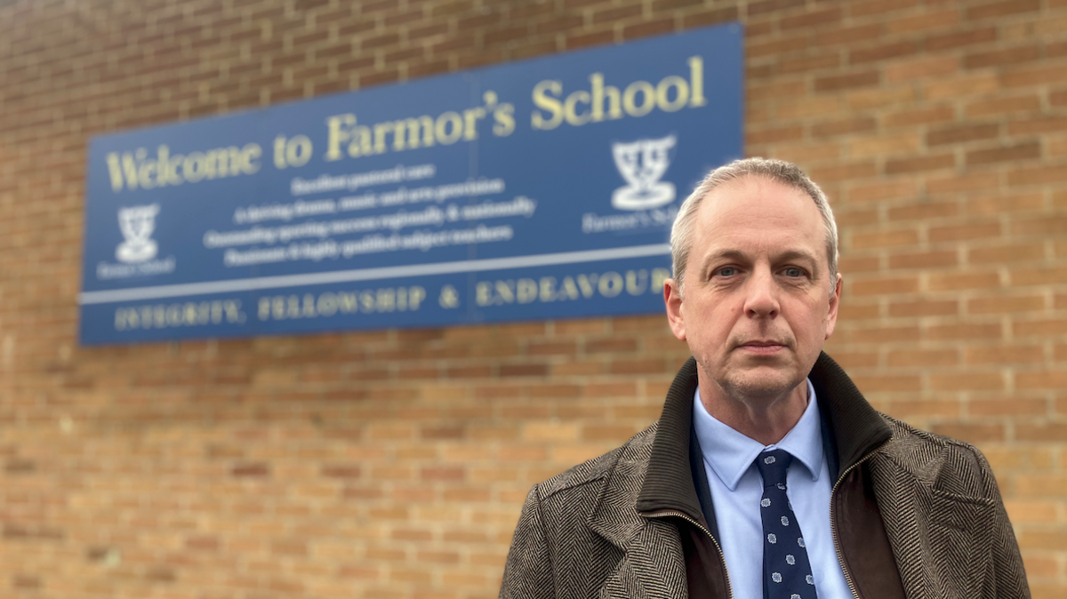 Man standing next to school sign 