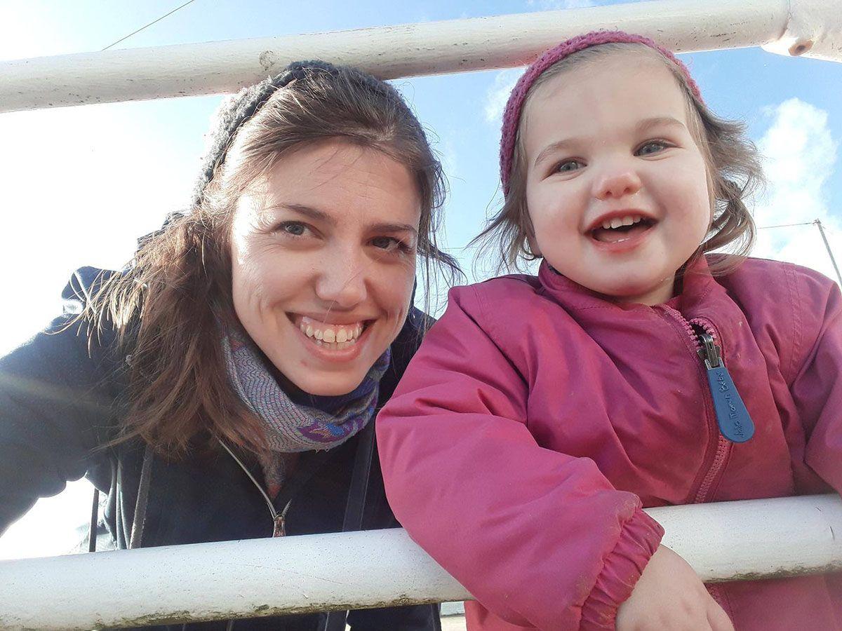 A woman and a young girl leaning in between two white railings smiling, blue sky in the background