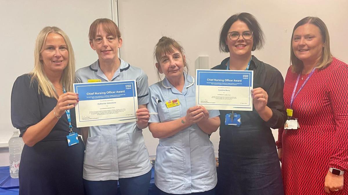 Kate and Caroline - wearing blue shirt uniform holding their certificates next two three other women staff members 