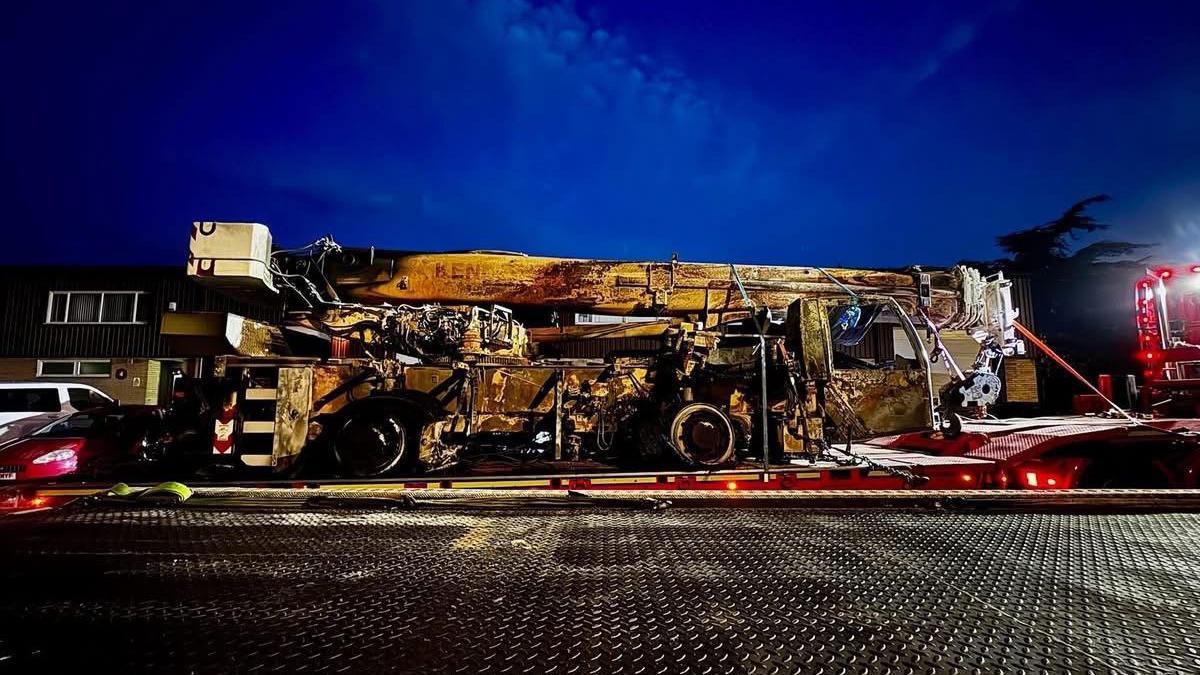 The damaged yellow crane is on the back on a lorry at night