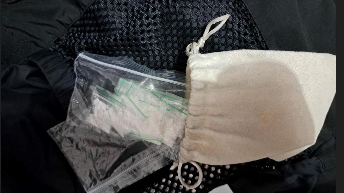 Cotton drawstring bag, open to display its content - a number of clear plastic wraps containing a white substance,  which police believe to be Class A drugs. It is resting on black webbed material, possibly the inside of a jacket