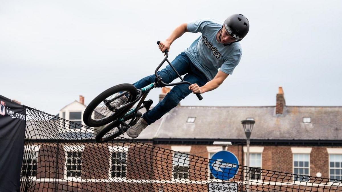 Man performing a demo on a bike during the festival. He is riding the bike on the edge of a fence. 