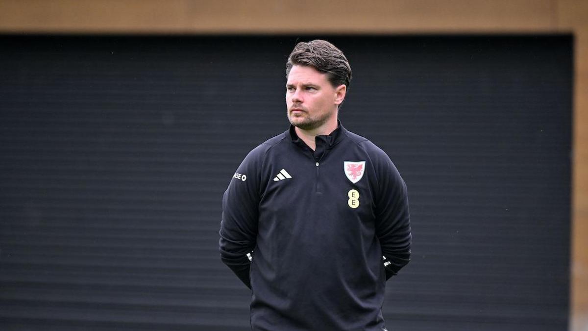 Drew Sherman standing with hands behind his back and looking to the side - he's wearing black Welsh training kit